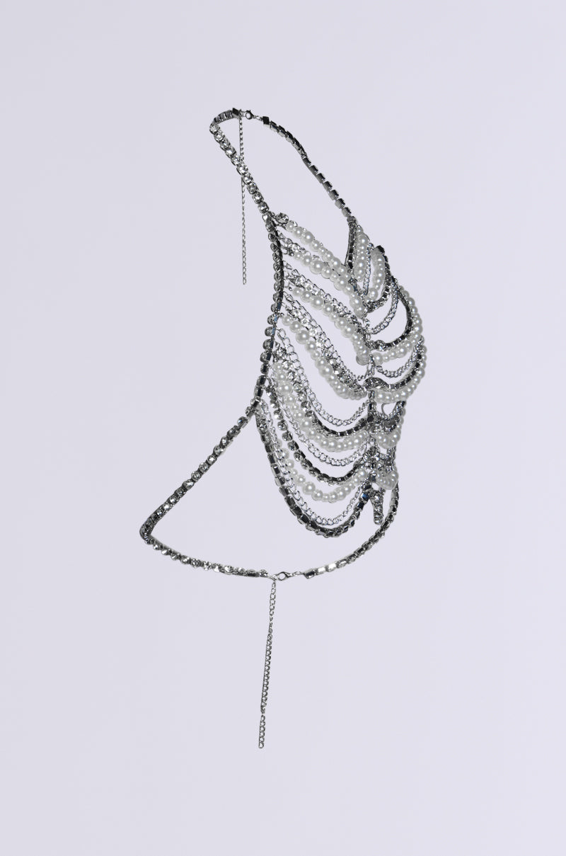 Side view of the EVA PEARL AND RHINESTONE BODY CHAIN featuring cascading loops and a thin chain hanging below, adding sparkle to its metallic bralette design. The halter-neck style beautifully stands out against a plain light gray background.