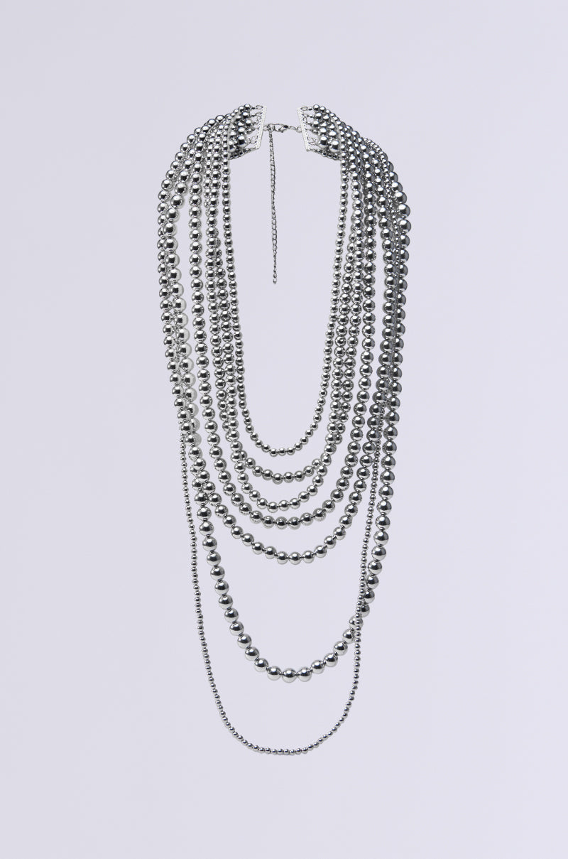 The ADORN ME LAYERED NECKLACE is a statement piece with multi-layered, metallic silver beads in varying lengths that cascade against a plain backdrop. 0