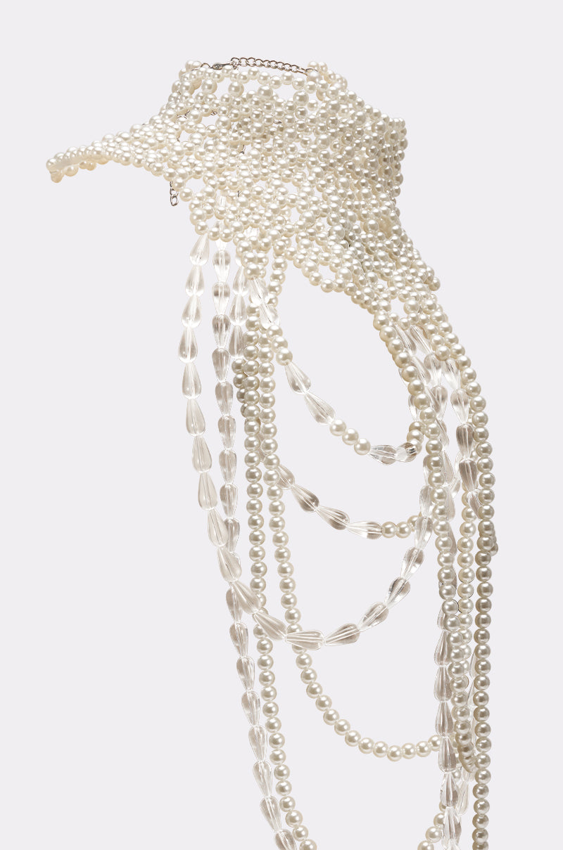 The ELEGANCE IS ME STATEMENT NECKLACE dazzles with cascading white pearl strands of varying lengths, creating a visor-like effect—an elegant accessory set against a plain light background. 6