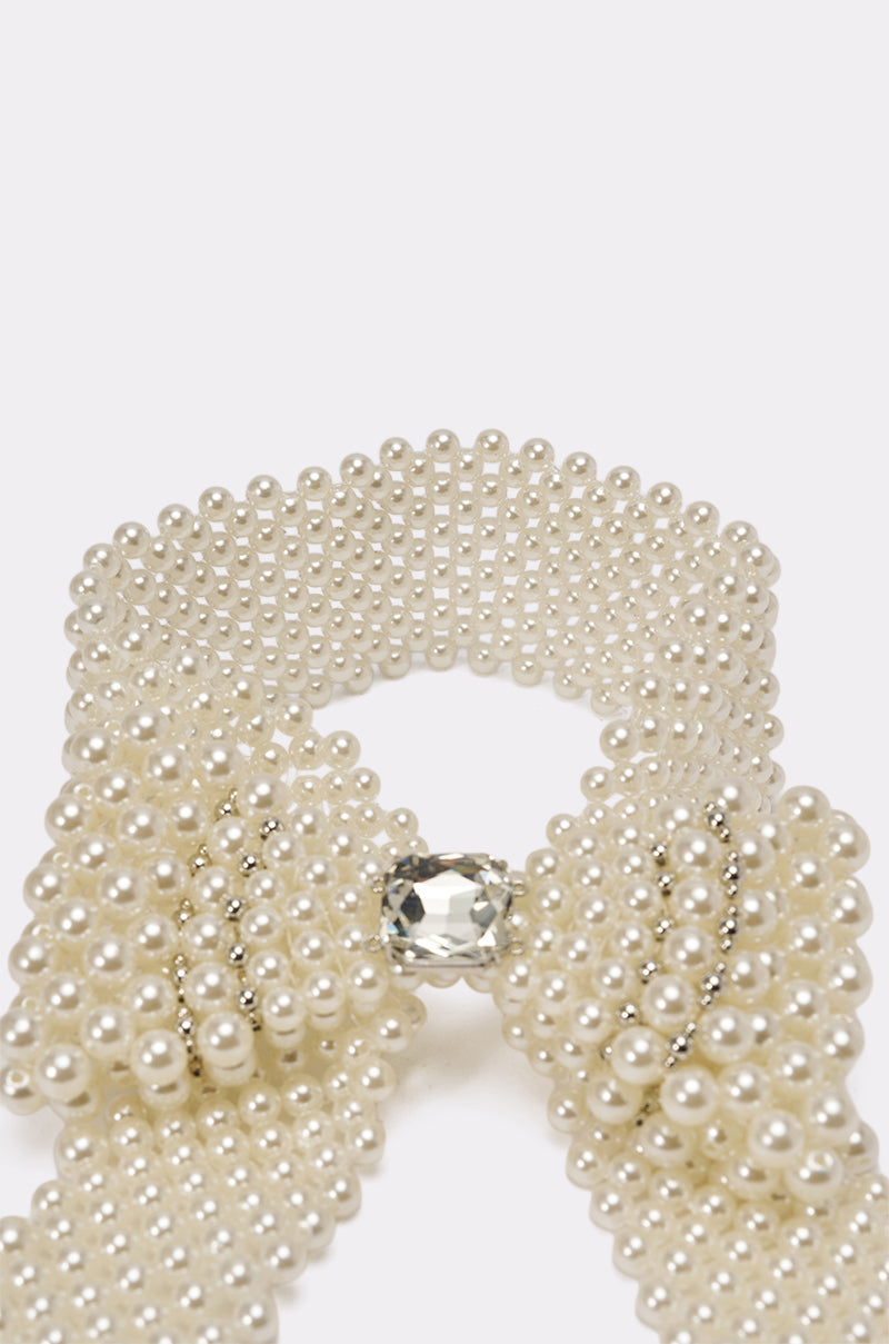 A close-up of the BUTTONED UP PEARL COLLAR, a vintage-inspired statement necklace featuring pearl beaded strands in a bow shape with a large clear gemstone at the center, displayed on a plain white background. 5