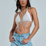 A woman confidently poses in a white rhinestone-adorned cowboy hat, a beaded halter top with pearl-like embellishments, the PEARL PLEASE BODY CHAIN by AKIRA Label, clear-framed glasses, and light blue jeans against a neutral background.