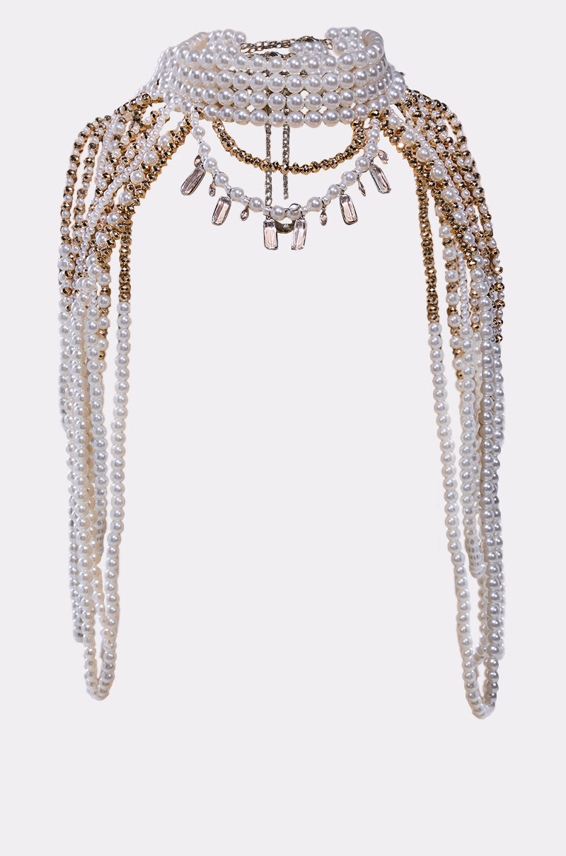 The OUT OF YOUR LEAGUE NECKLACE displays layered strands of white pearls and gold beads with clear gemstone accents, creating an intricate, draped choker design against a plain background.