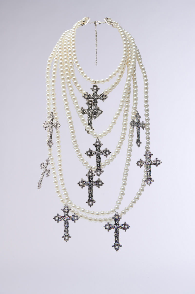 The PROTECTED LAYERED CROSS NECKLACE features multiple strands of faux pearls and ornate silver-tone crucifix pendants, creating a striking layered look against a plain light background. 0