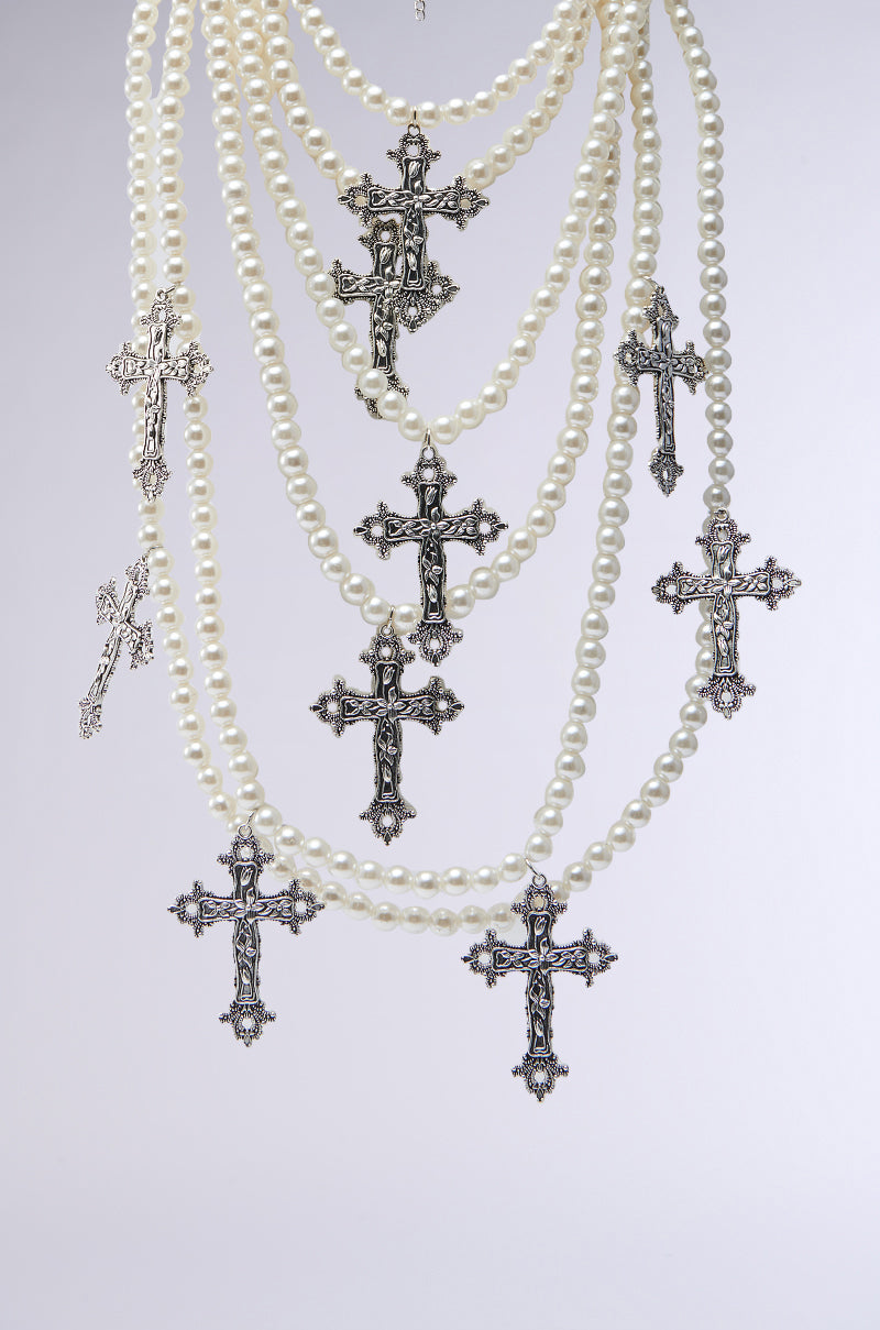 The PROTECTED LAYERED CROSS NECKLACE features multiple strands of faux pearls and ornate silver-tone crucifix pendants, beautifully layered and showcased against a simple light background. 2