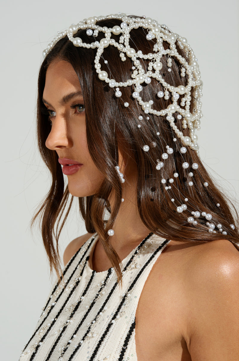 A person with long brown hair is wearing a PEARL LOVE HEADPIECE embellished with cascading pearl beads, complementing their sleeveless striped top against a plain backdrop.
