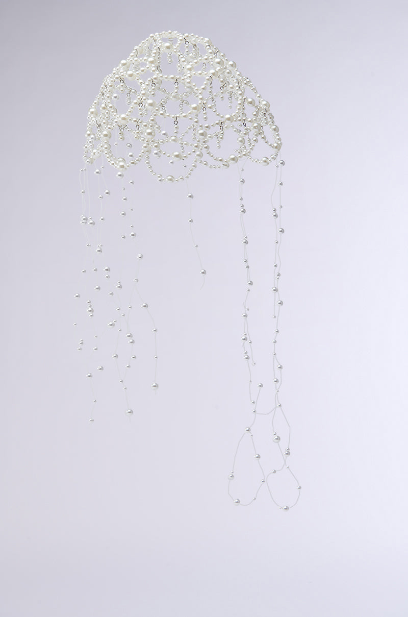 The PEARL LOVE HEADPIECE is a delicate sculpture crafted from silver wire and pearl beads. It has an airy, intricate round top with cascading strands resembling tentacles, beautifully showcased against a plain white background.