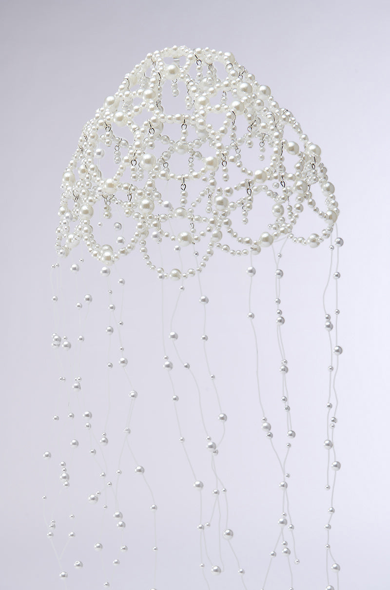 The PEARL LOVE HEADPIECE is a delicate sculpture with pearl beads hanging from thin wires on a soft gray base, resembling jellyfish tentacles with its cascading curved patterns.
