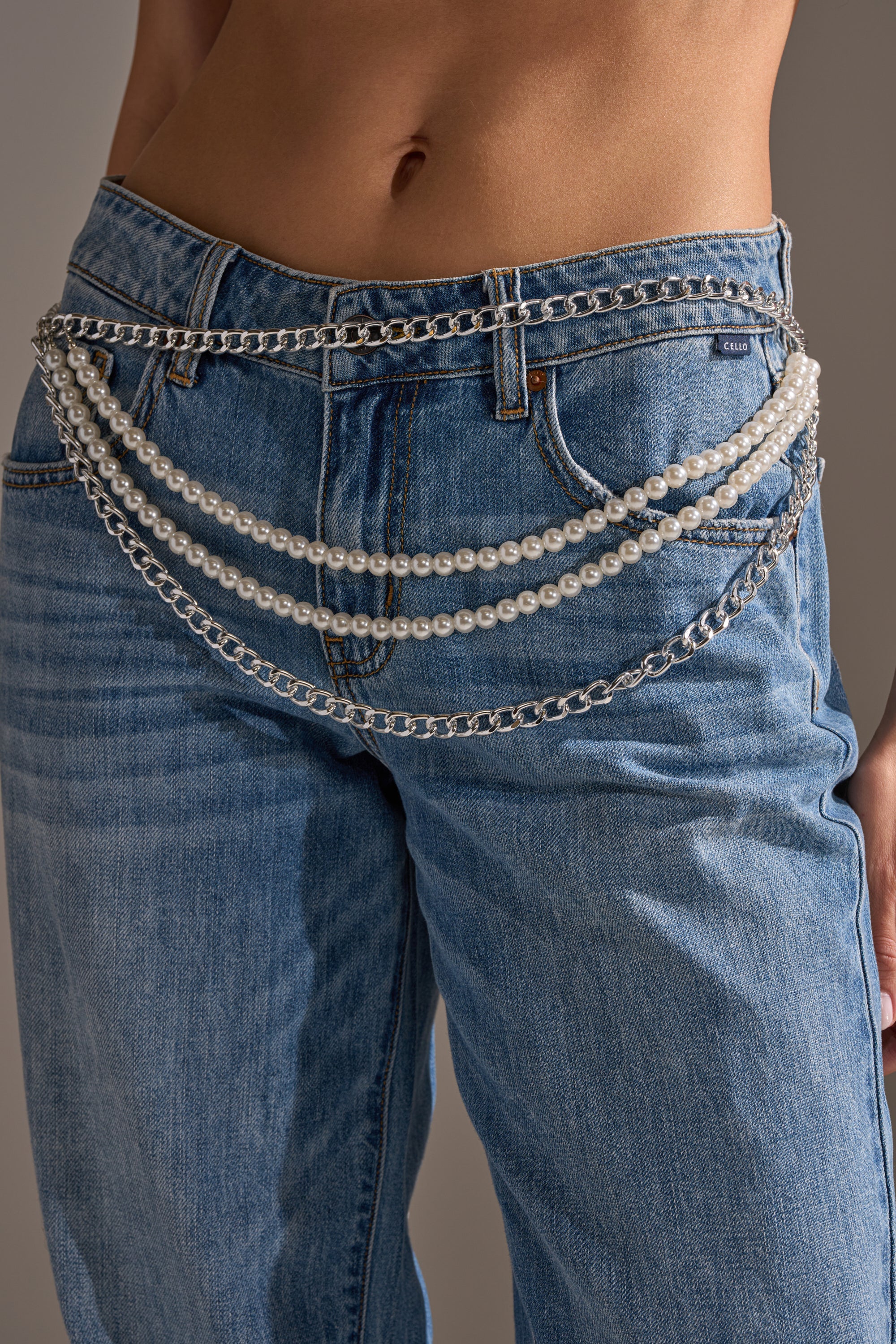 A person in low-rise blue jeans accessorized with BELT—a pearl chain hip belt featuring layered silver chains and pearl strands draped across the front. 2