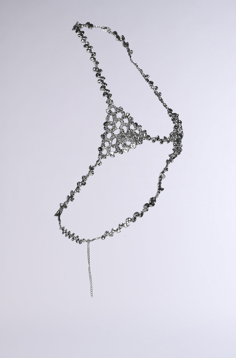The KEL BODY CHAIN is intricately designed with a triangle shape, featuring hammered silver beads and elaborate loops. It hangs gracefully on a plain gray background, complete with a delicate chain cascading from one end. 7