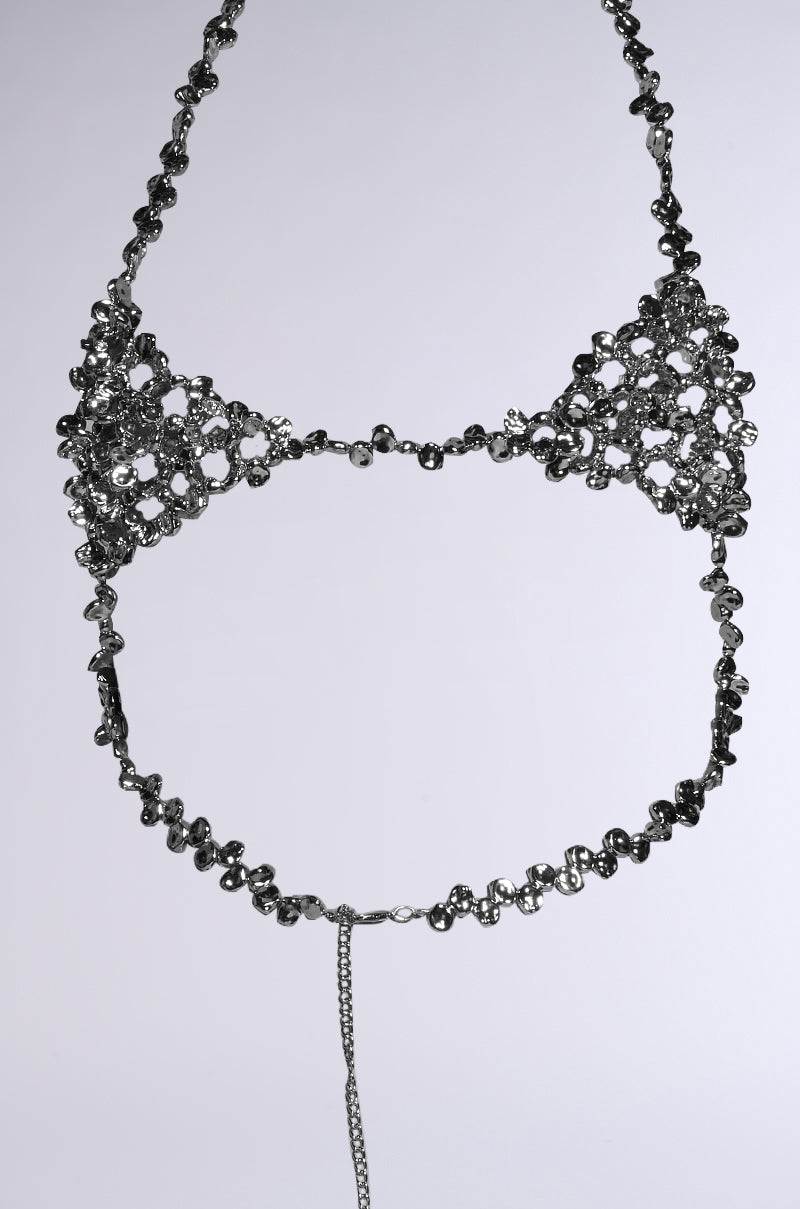 The KEL BODY CHAIN is a metallic halter-style accessory with an intricate floral pattern, adorned with hammered silver beads. It features connected loops and a central string that elegantly extends downwards, set against a plain grey background. 8