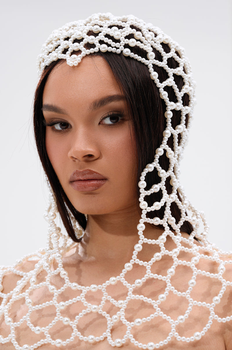 A woman with straight dark hair wears the ELEGANT VIBES PEARL HEADPIECE and a white pearl top, set against a plain light background. She gazes confidently at the camera, embodying elegance.
