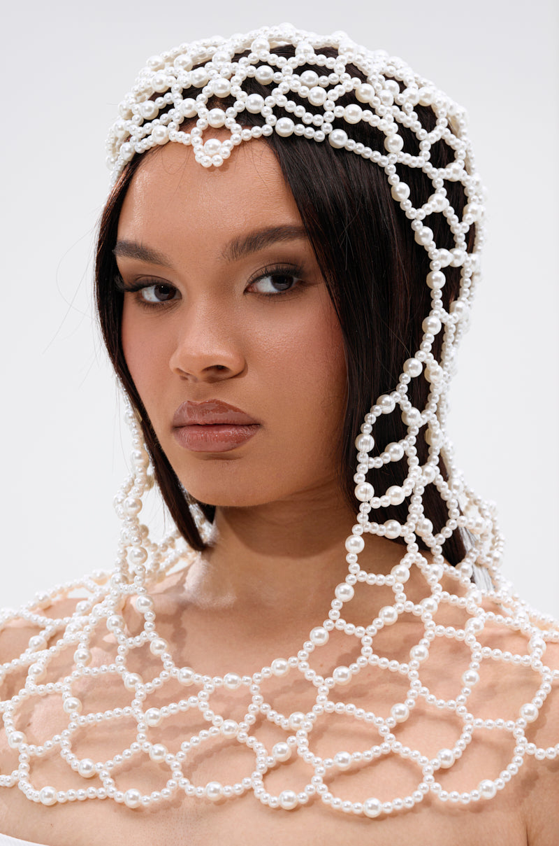 A woman with straight dark hair wears the ELEGANT VIBES PEARL HEADPIECE, an intricate net-patterned accessory elegantly draped over her head and shoulders. She has a neutral expression and smooth, even-toned complexion.