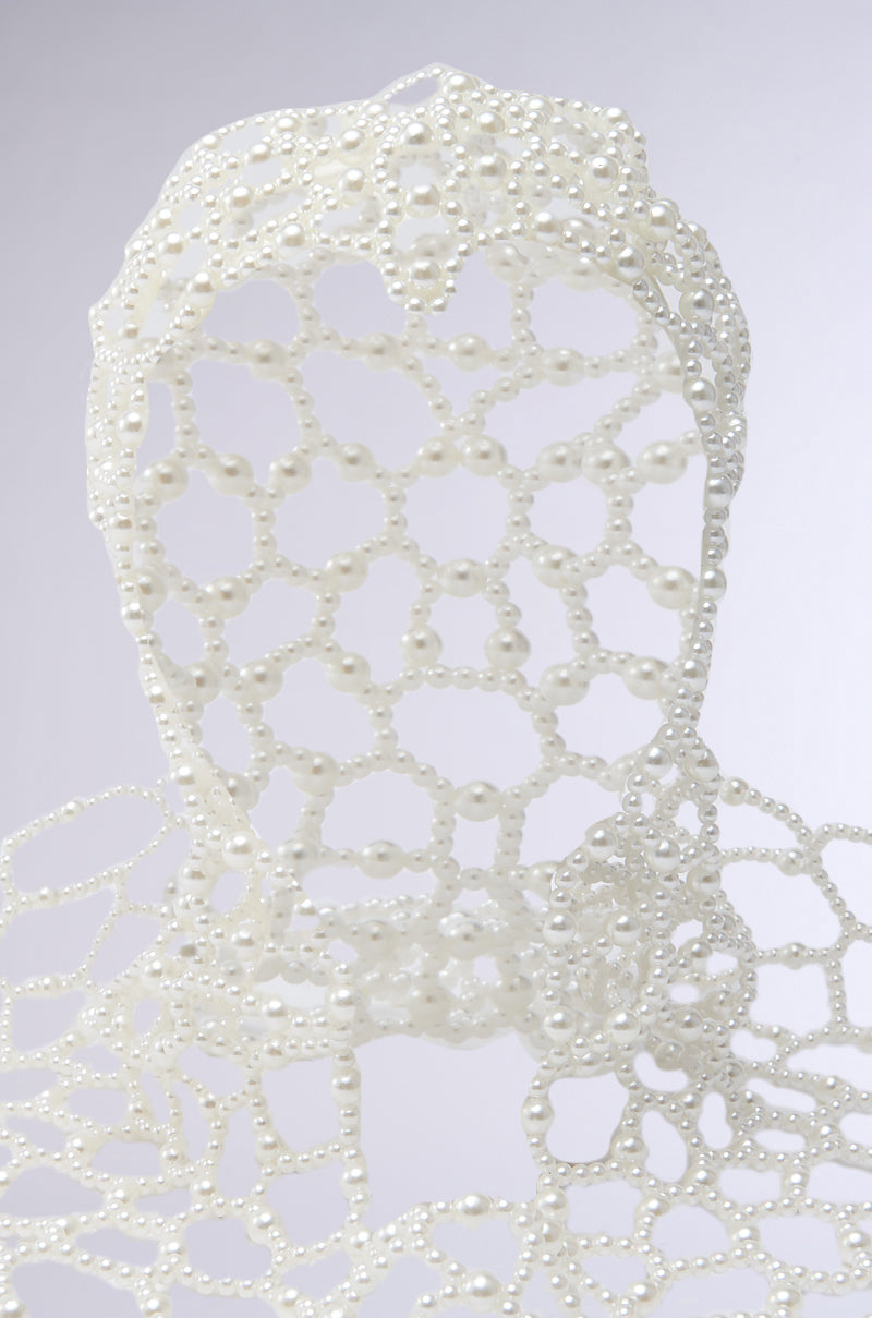 The ELEGANT VIBES PEARL HEADPIECE features an abstract human bust formed from interconnected white pearls in a mesh-like design, set against a simple light background for a chic, high-fashion look.