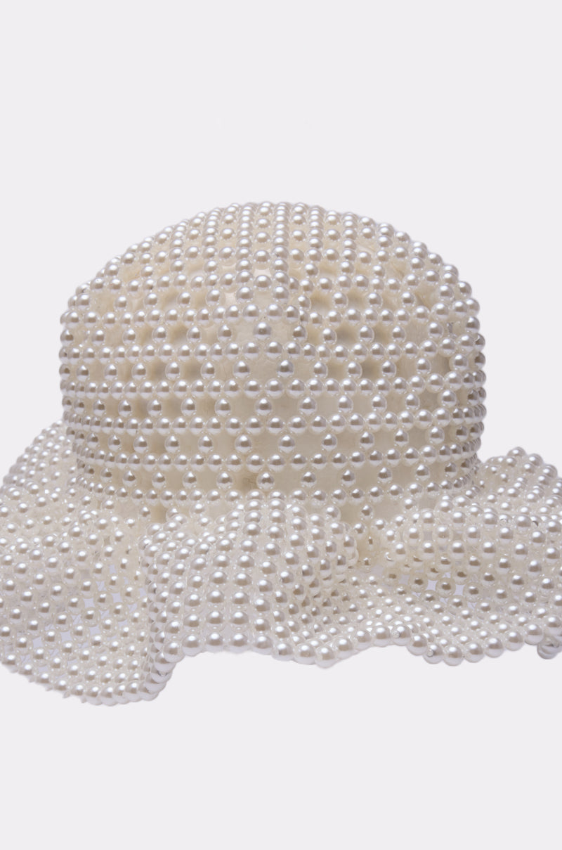 The PEARL DREAMS BUCKET HAT features a rounded crown and wide, wavy brim, adorned with rows of shiny pearls, set against a plain light background. 4