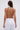 A woman with long brown hair, seen from the back, wears white pants and the CLEOPATRA RHINESTONE CHAIN TOP featuring silver chain straps with gemstone details on the shoulders. The plain background is light-colored.