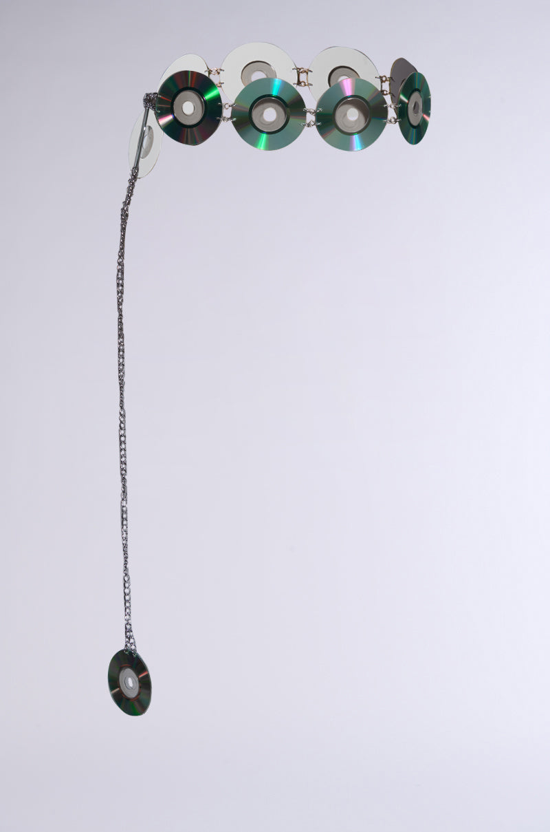 The PLAY IT AGAIN CD BELT is a unique artwork with holographic CD discs linked in a circle, featuring a chain elegantly extending to another disc, beautifully photographed on a light gray background reminiscent of Y2K accessory belts.