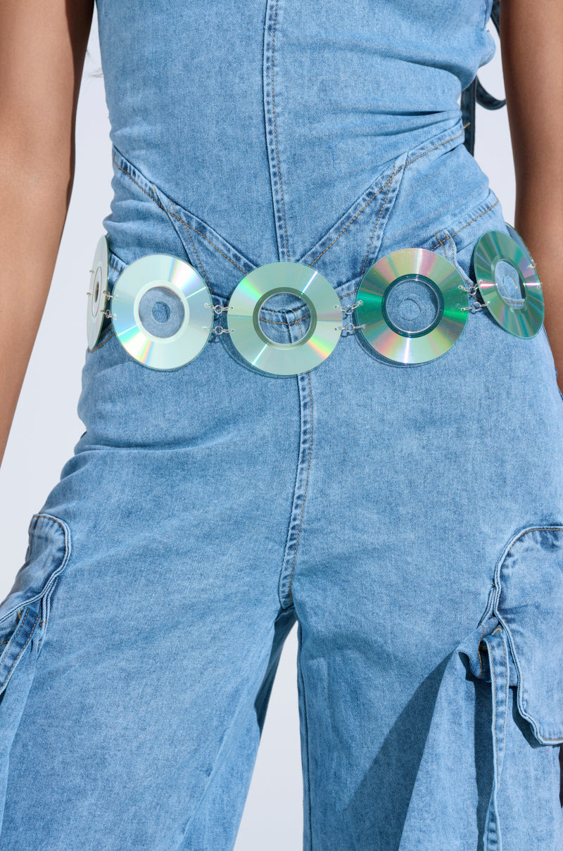 Wearing a denim outfit paired with the PLAY IT AGAIN CD BELT, featuring shiny holographic CDs, creates a nostalgic Y2K look. Sunlight reflects off the discs for a vibrant effect. The ensemble is completed with detailed stitching and side pockets.