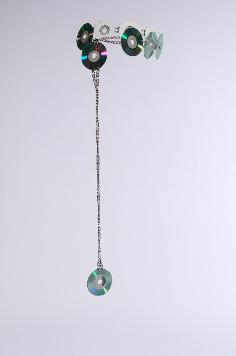 The PLAY IT AGAIN CD BELT features holographic CD discs forming a circular sculpture, linked by metal chains. It channels Y2K nostalgia with a single dangling disc against a plain white background.