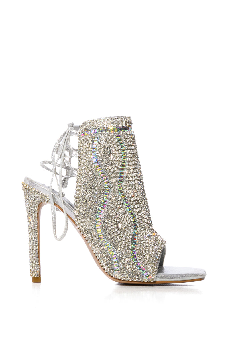 The AZALEA WANG DELANIE SILVER STILETTO SANDAL dazzles with an open toe, lace-up back, and rhinestone-embellished wavy crystal patterns, adding glamour to any outfit.