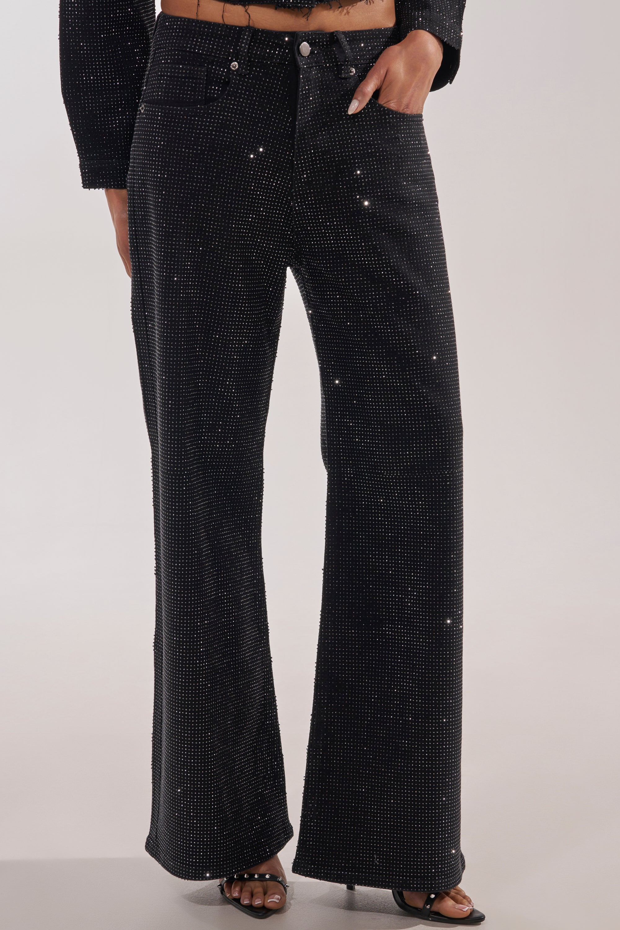 Model wearing the DEMI EMBELLISHED RELAXED DENIM IN BLACK, high-waisted jeans adorned with rhinestones, styled with open-toed heels. Photo shows from chest down against a plain background. 5