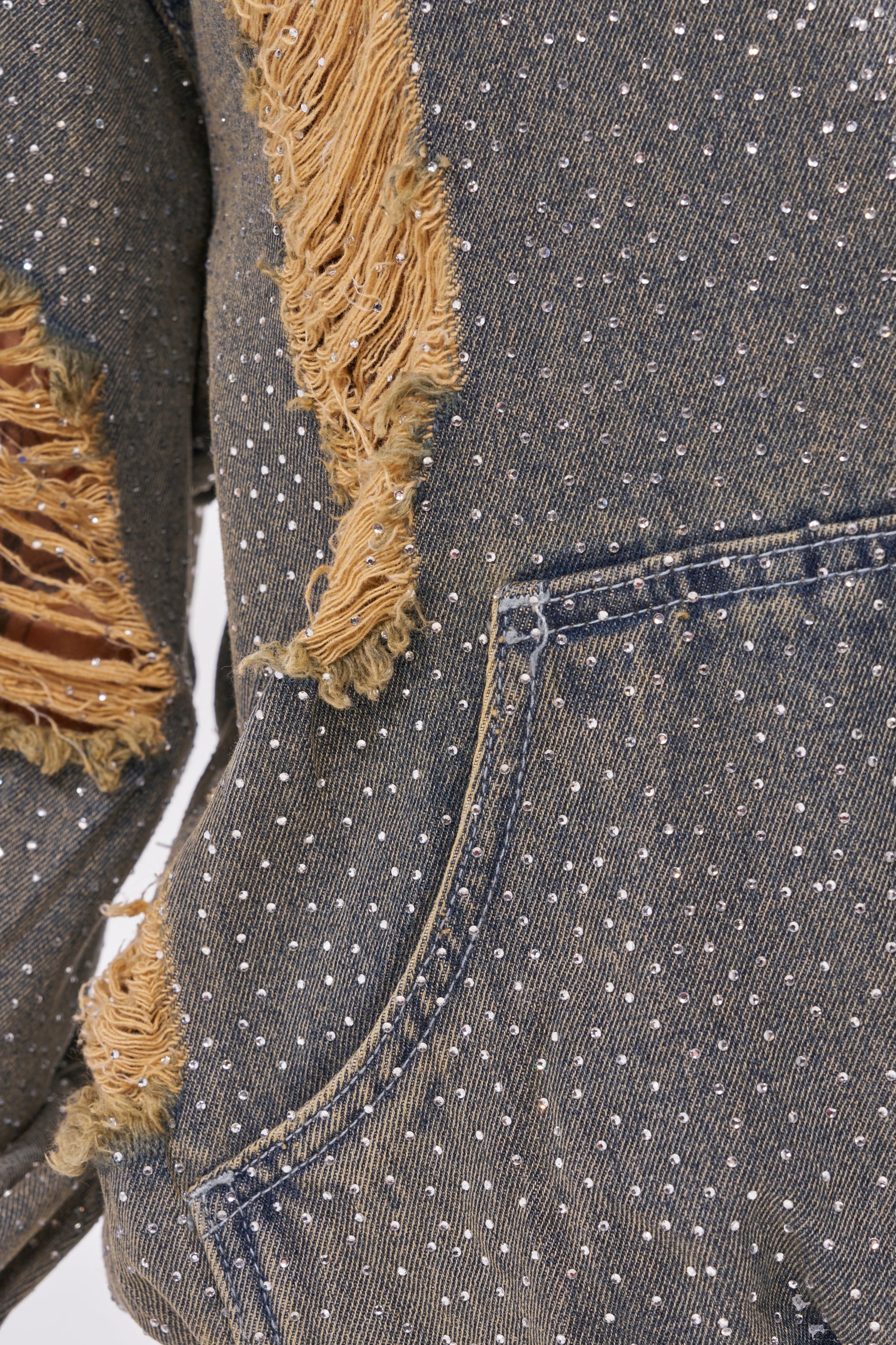 Close-up of the DEMI RHINESTONE DENIM HOODIE featuring distressed denim with frayed patches, white polka dots, detailed stitching, and a pocket edge—ideal for adding festival streetwear flair to your look. 9