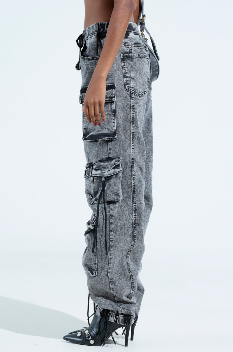 Model wearing the LOOKS FIRE DENIM JOGGER with cargo pockets and drawstring ties, paired with black pointed shoes featuring metal accents and a small heel. The side profile is captured against a simple background.
