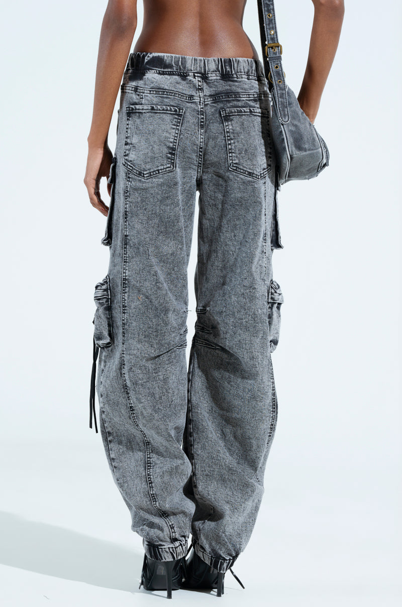 A person is wearing the LOOKS FIRE DENIM JOGGER, loose-fitting gray cargo jeans with multiple pockets, viewed from the back. They’re carrying a matching gray denim bag on their shoulder and finishing the look with black footwear.