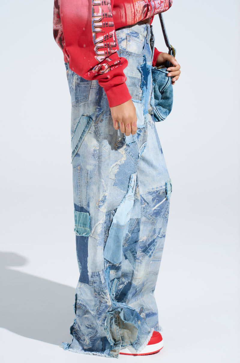 Someone is wearing DENIM ON DENIM PATCHWORK JEANS with frayed edges in blue hues, paired with a red and white long-sleeve top, red sneakers, and holding a denim handbag. The background is plain and light-colored.
