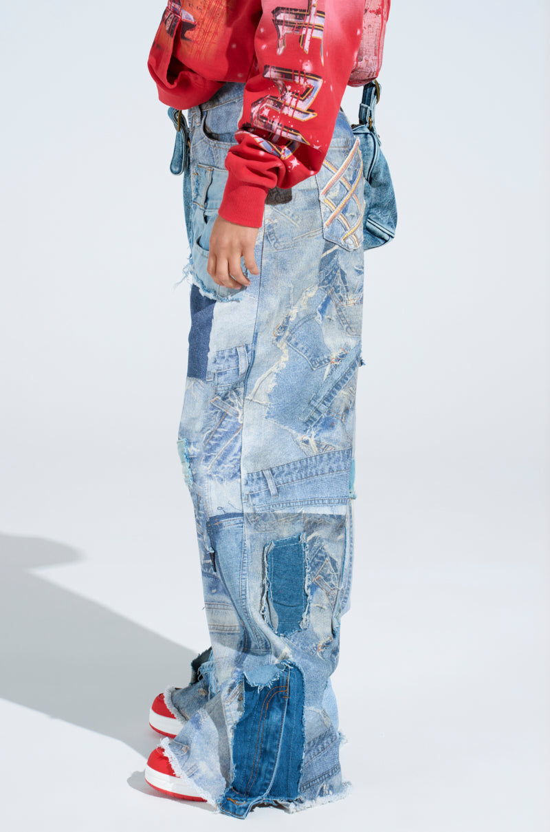 Someone sports DENIM ON DENIM PATCHWORK JEANS, featuring high-rise wide legs in varied blue tones with unique stitching and distressed detailing. They're styled with a red sweatshirt and matching red-and-white sneakers against a light backdrop.