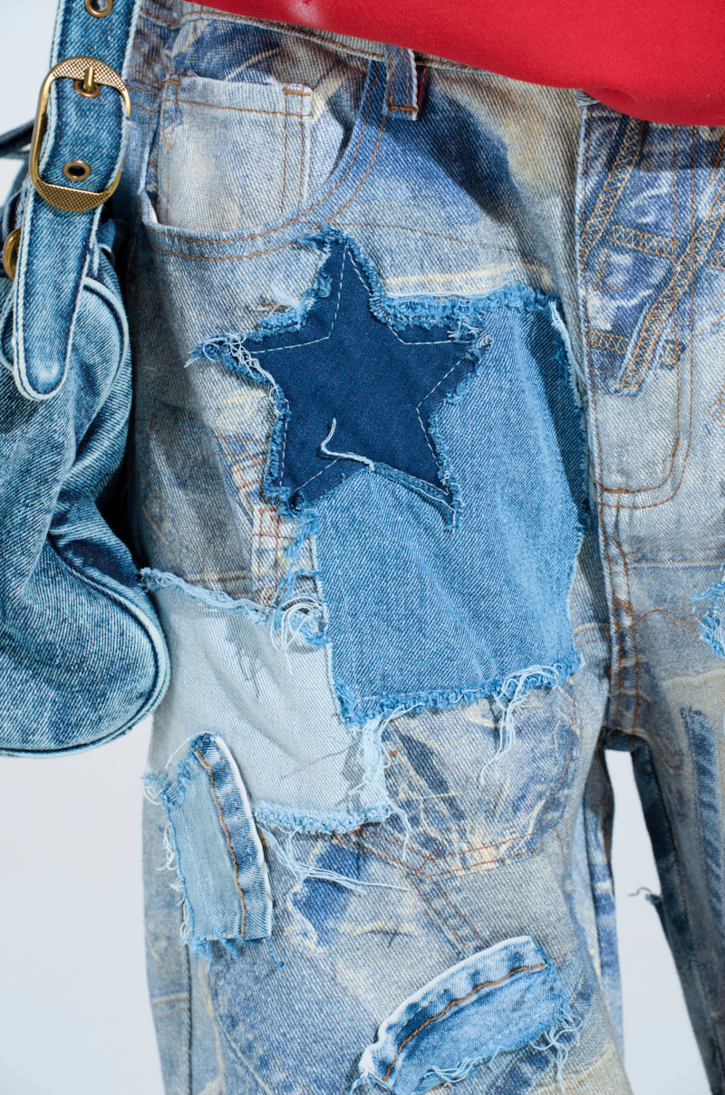 A person wears the DENIM ON DENIM PATCHWORK JEANS featuring distressed patchwork with a prominent dark star, paired with a blue bag with gold buckles. The high-rise wide-leg jeans have a frayed look, complemented by a glimpse of a red top.