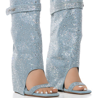 Two legs in the AZALEA WANG DESARAY Rhinestone Open Toe Wedge Bootie, featuring glittery light blue, knee-high, open-toe boots with a chunky wedge heel and shin-high fold-over design adorned with rhinestones for a chic denim sandal bootie effect.