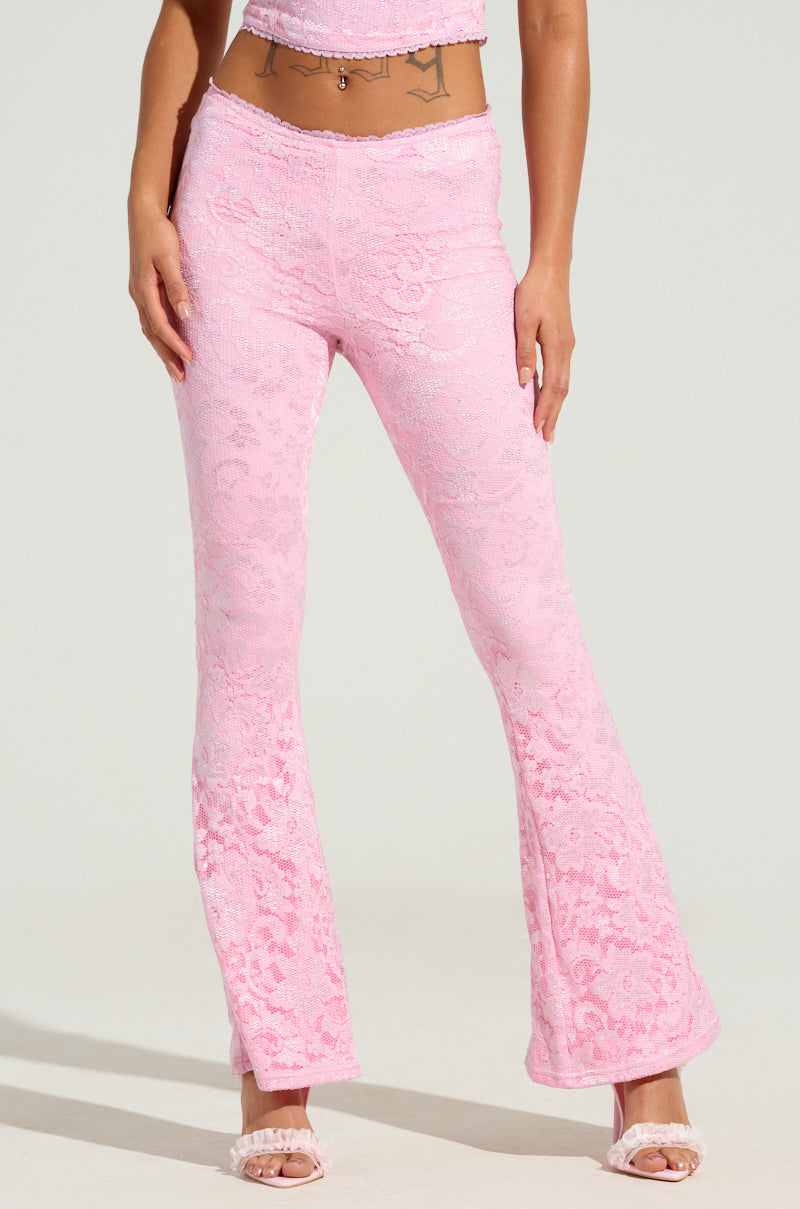 Wearing the "LIKE LAST TIME FLARE PANT," a high-rise pink flare pant set featuring floral lace designs is paired with a coordinating crop top. The look is finished with open-toed sandals, set against a simple, light-colored backdrop.