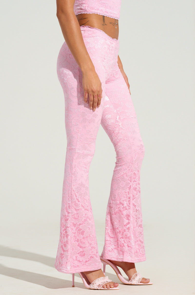 A person wearing the LIKE LAST TIME FLARE PANT in a floral lace pattern, paired with a matching pink crop top, stands in profile to showcase the intricate design of the ensemble. The look is completed with pink high heels against a simple, light background.