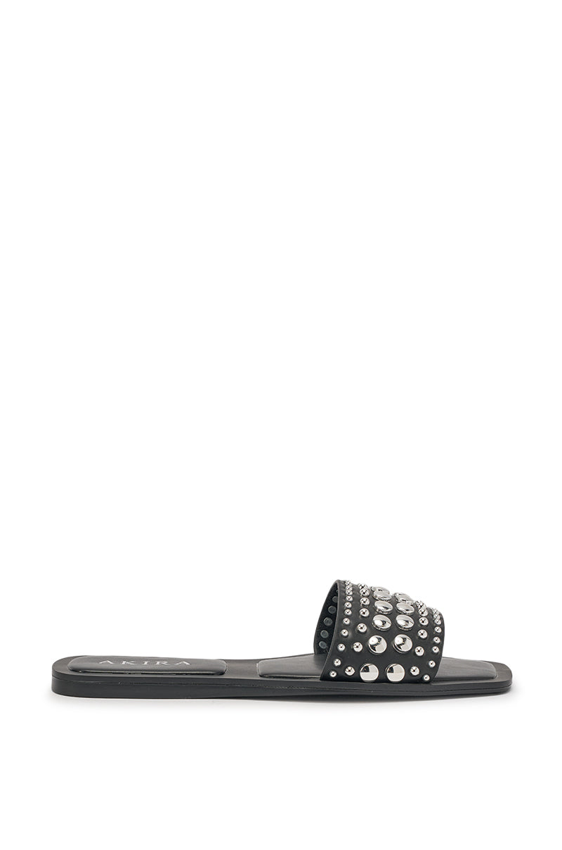 The AKIRA DEVORA BLACK HARDWARE EMBELLISHED FLAT SLIP ON SANDAL features a wide faux leather strap with silver studs and rhinestones. This black open toe sandal is displayed on a plain white background. 4