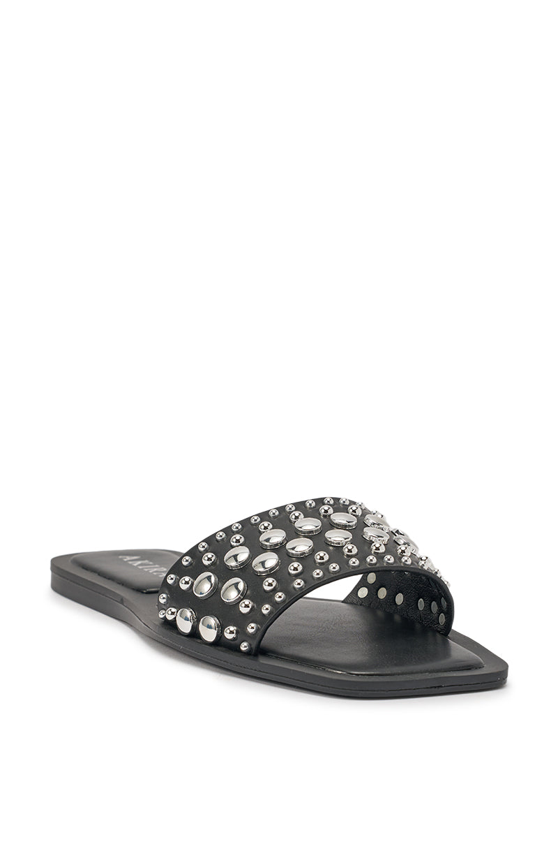 The AKIRA DEVORA Black Hardware Embellished Flat Slip On Sandal features a wide black faux leather strap decorated with large and small silver studs and rhinestones, shown against a white background. 5