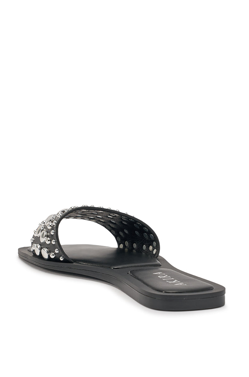 The AKIRA DEVORA Black Hardware Embellished Flat Slip On Sandal features a wide black strap with silver and clear studs and gems, shown from a rear side angle against a white background. 6