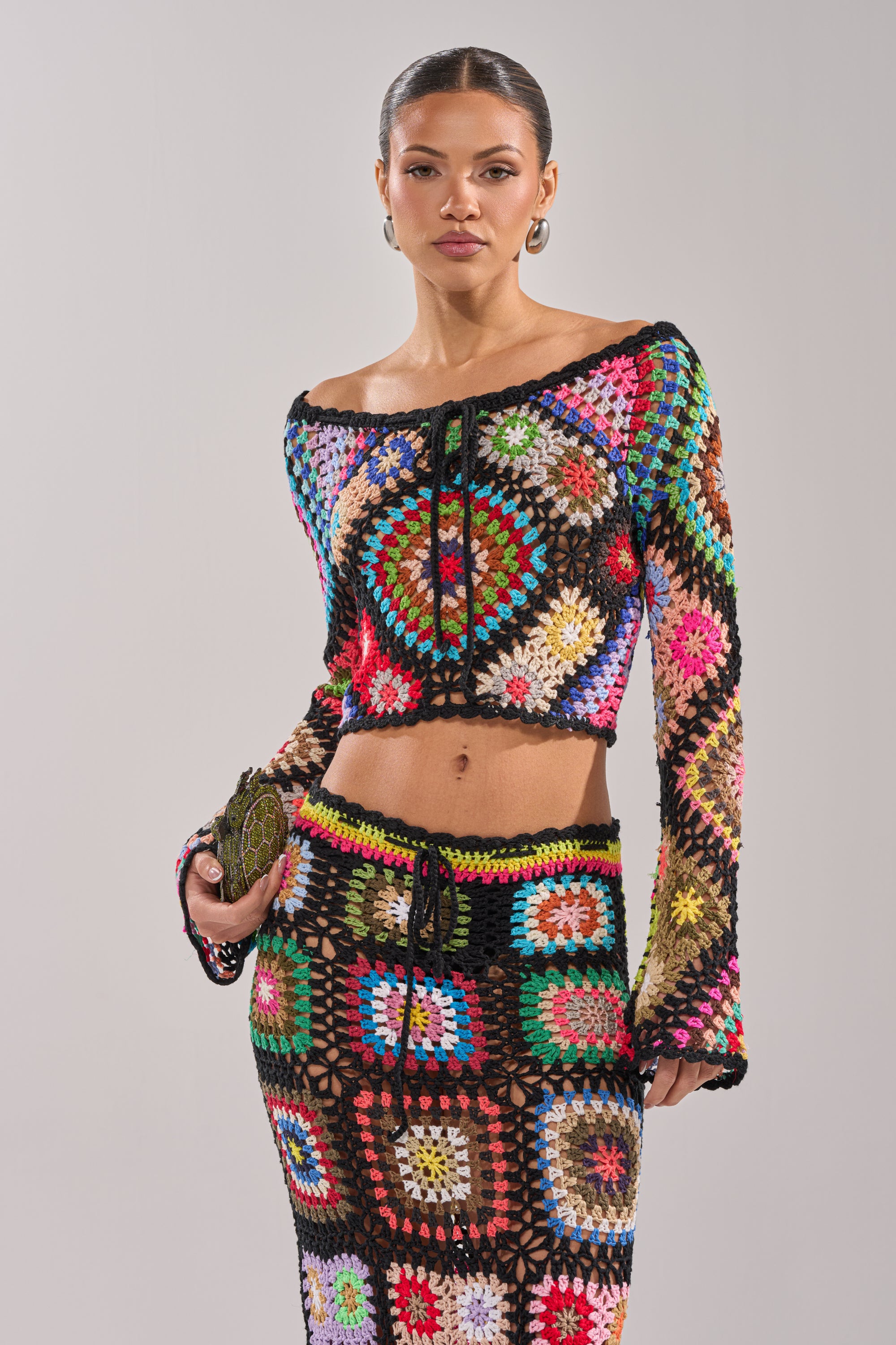 A woman models the SHINE ON YOU CROCHET TOP and matching skirt, both with vibrant granny-square patchwork, standing against a plain background—perfect for a festival look. 0