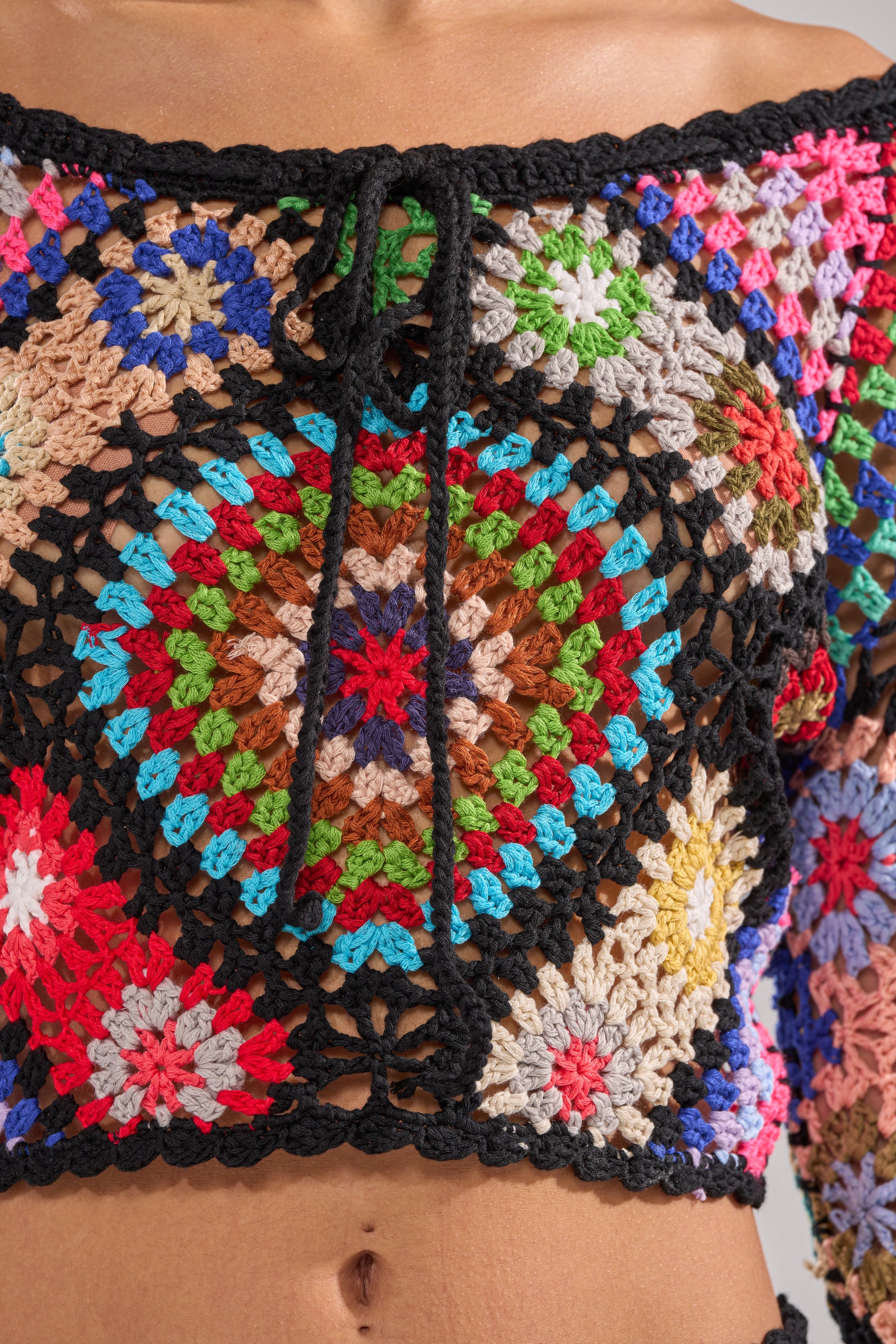 The SHINE ON YOU CROCHET TOP is a vibrant festival piece with a circular mandala design, black borders, and neckline ties. Its granny-square patchwork pops in lively red, green, blue, pink, and beige. 9