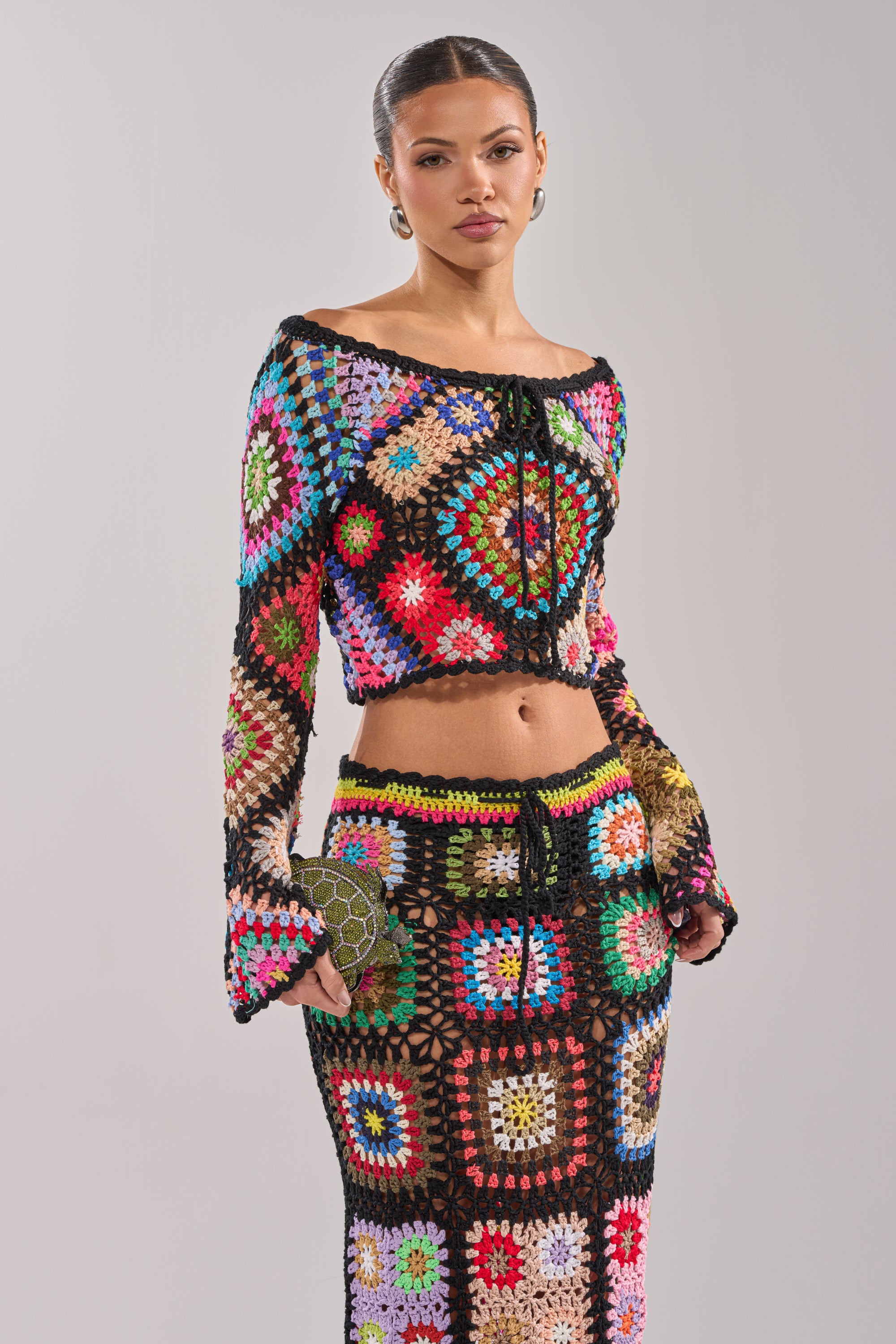 A woman wears the SHINE ON YOU CROCHET TOP with a matching skirt, creating a vibrant festival look. She holds a small clutch and stands against a plain background. 2
