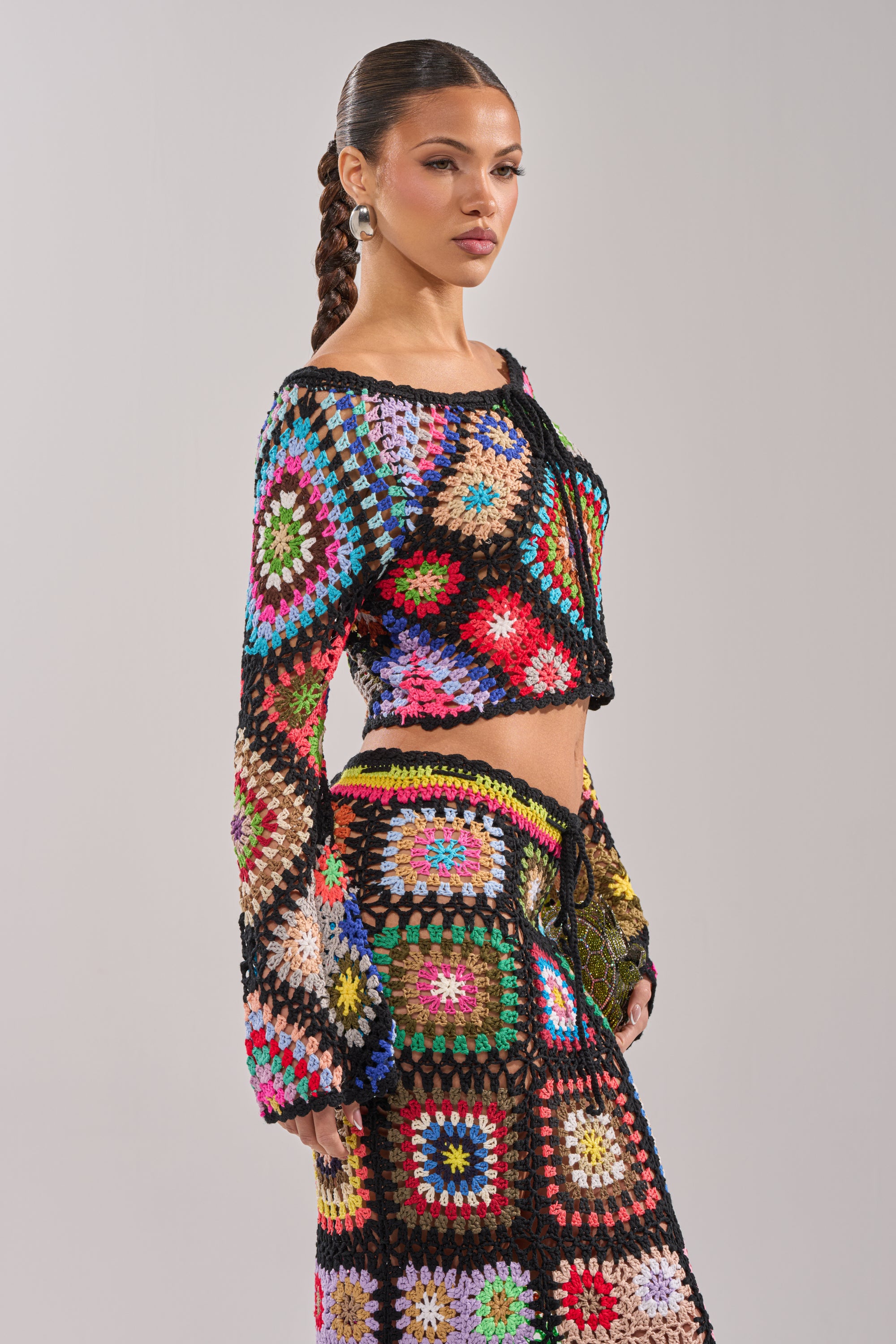 Wearing the SHINE ON YOU CROCHET TOP and a matching skirt, a woman creates a bold festival look as she stands against a plain light background. 4