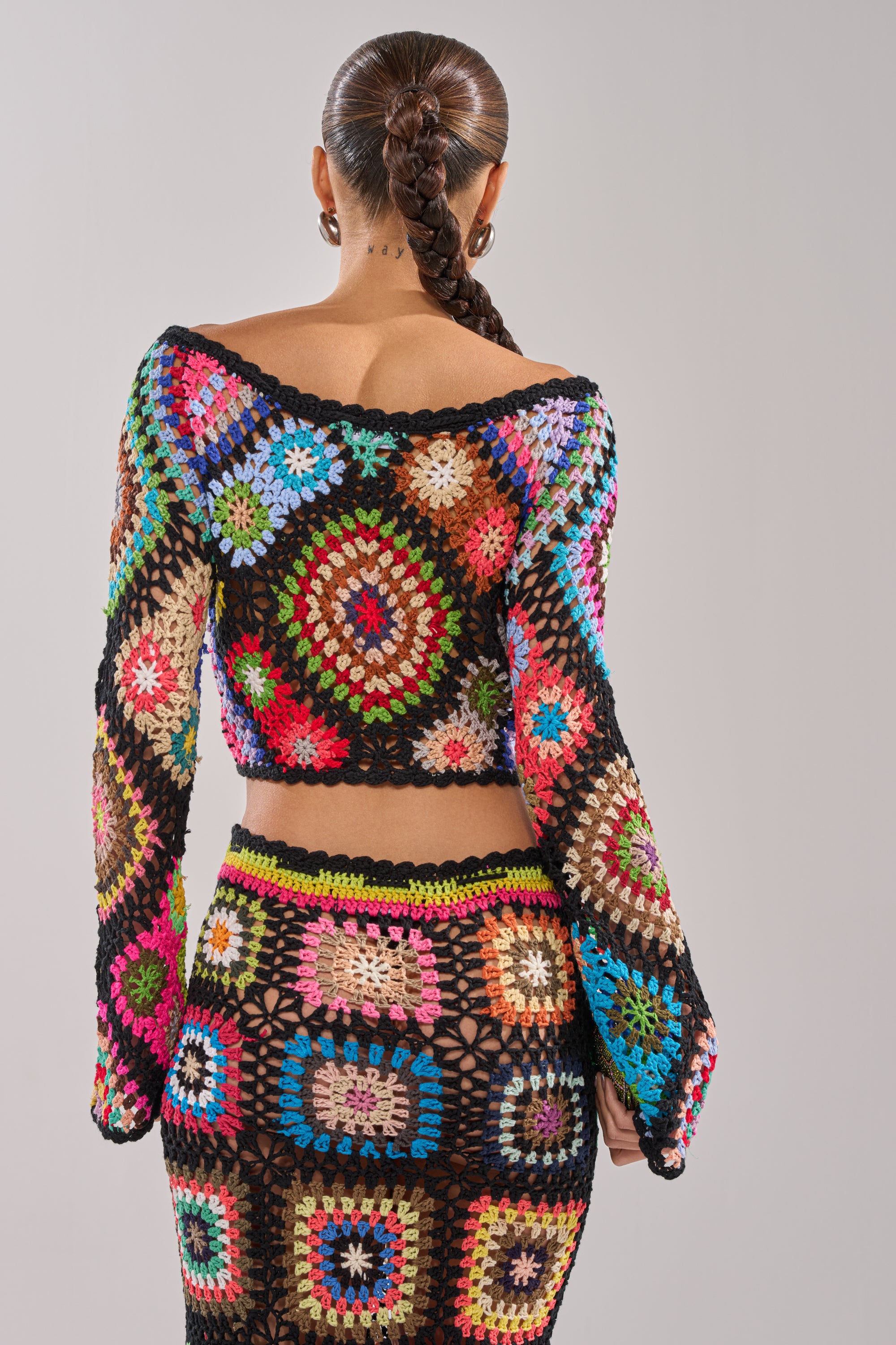 A woman with a long braided ponytail is seen from behind, wearing the SHINE ON YOU CROCHET TOP and matching skirt in vibrant granny-square patchwork, with black borders and bold colors for a standout festival look. 5