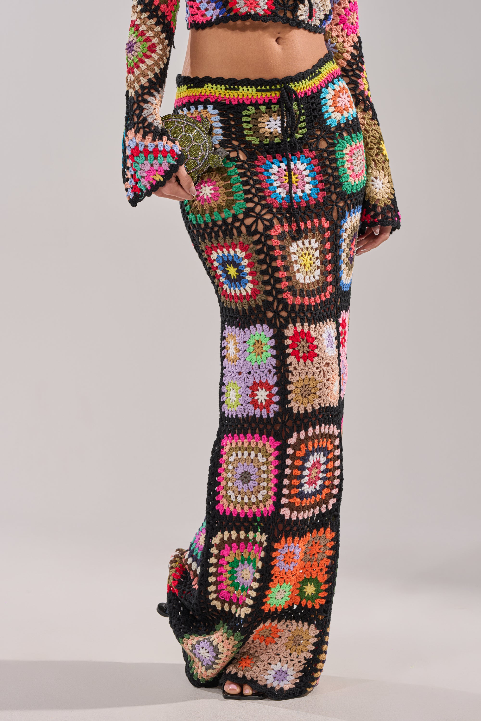 Wearing the SHINE ON YOU CROCHET MAXI SKIRT, a high-rise fitted maxi in vibrant granny-square crochet, paired with a matching long-sleeve crop top. The face is not visible against the plain background. 1