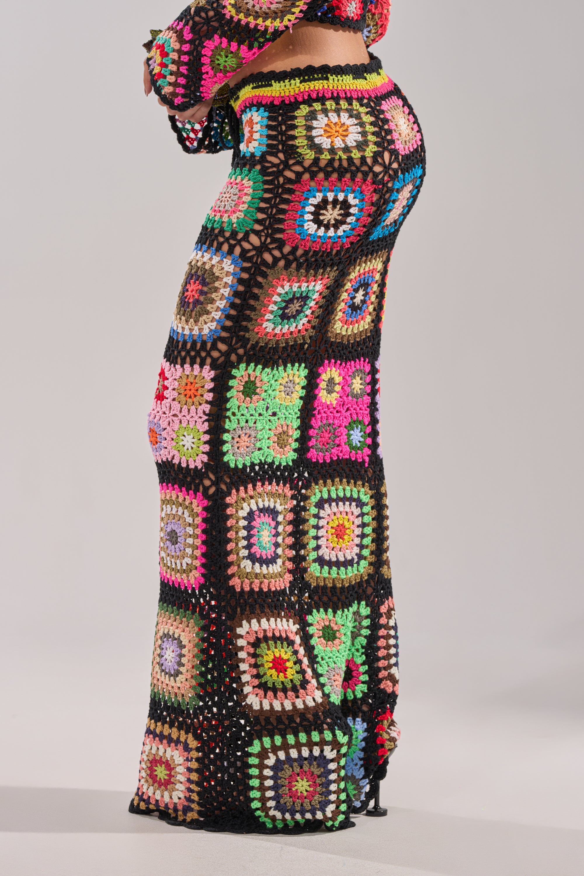 The lower half of a person is shown against a plain light background, wearing the SHINE ON YOU CROCHET MAXI SKIRT—a high-rise crochet maxi skirt featuring colorful granny-square patchwork with black borders. 3