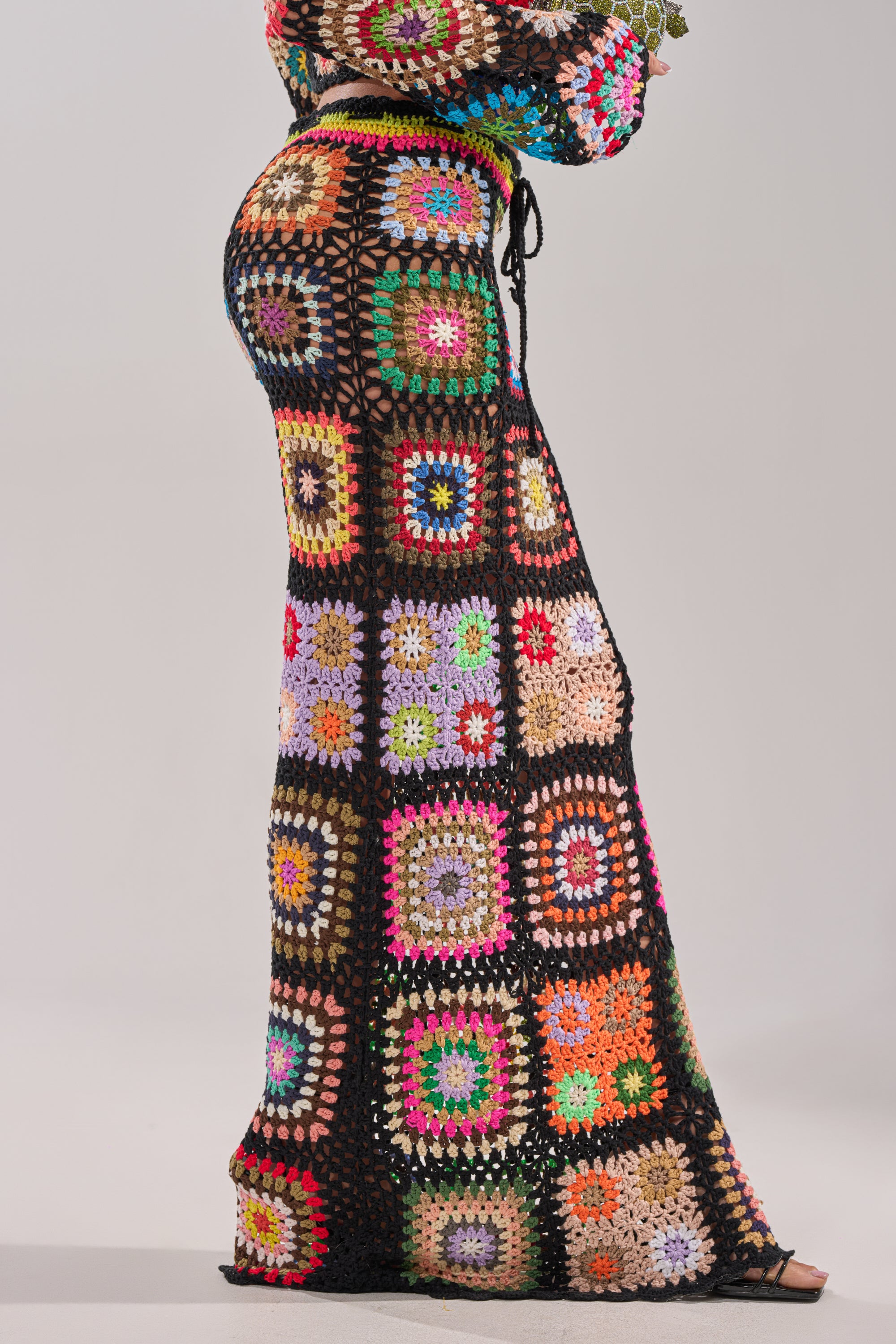 A person wears the SHINE ON YOU CROCHET MAXI SKIRT, a colorful high-rise maxi with multicolored granny-square patchwork bordered in black, standing against a plain light background. 4
