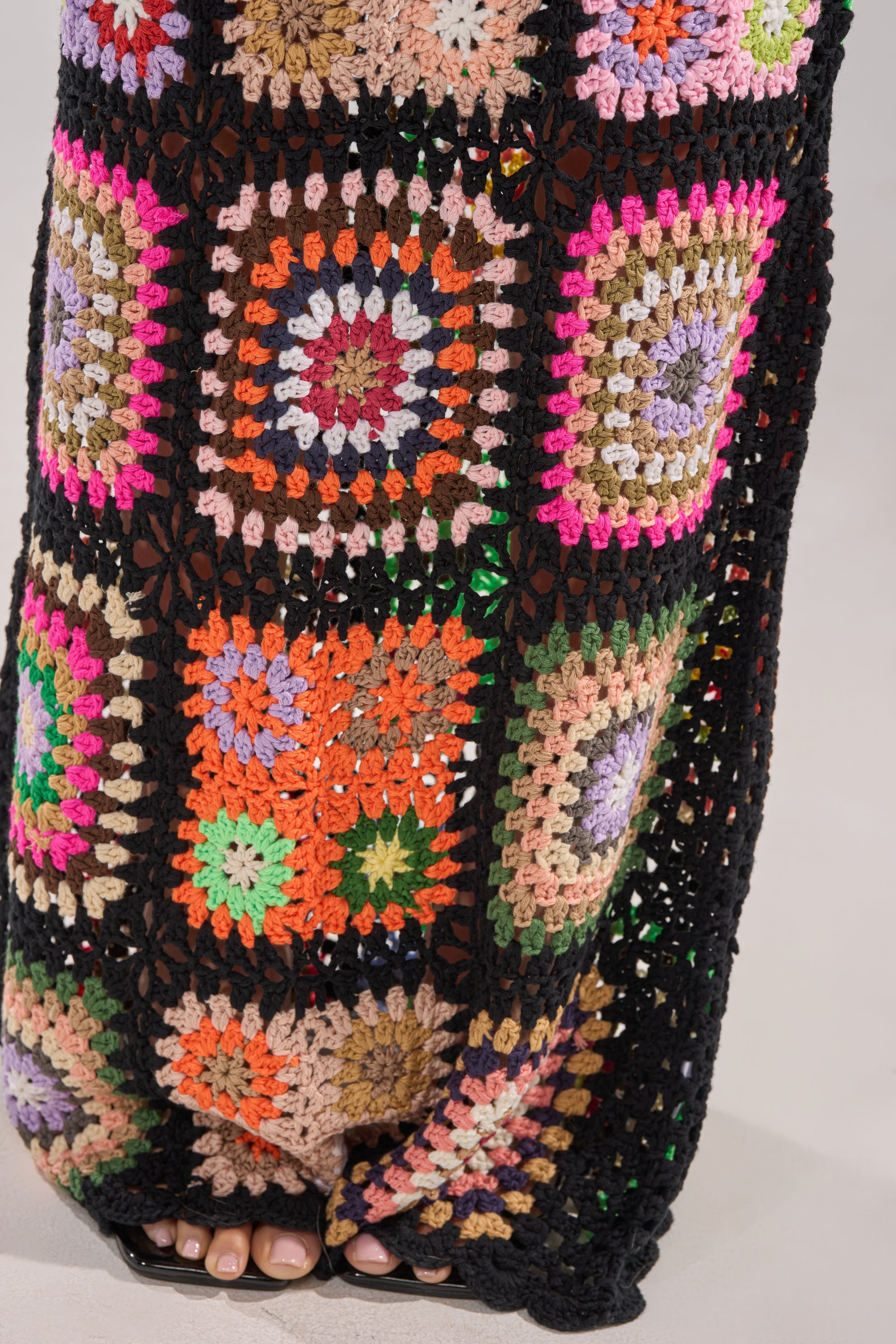 A close-up of vibrant granny-square patchwork evokes the detailed craftsmanship of the SHINE ON YOU CROCHET MAXI SKIRT, with black borders and toes peeking out for a cozy, charming touch. 8