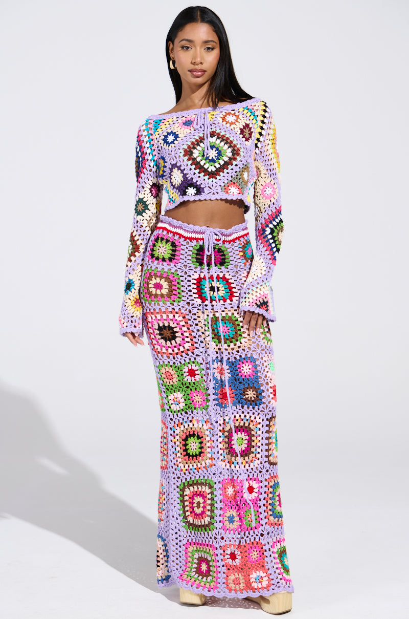 A woman models the "SHINE ON YOUR CROCHET MAXI SKIRT," featuring a colorful crochet design with geometric and floral patterns on a neutral base. The breezy high-rise fit captures summer style and confidence against a plain background.