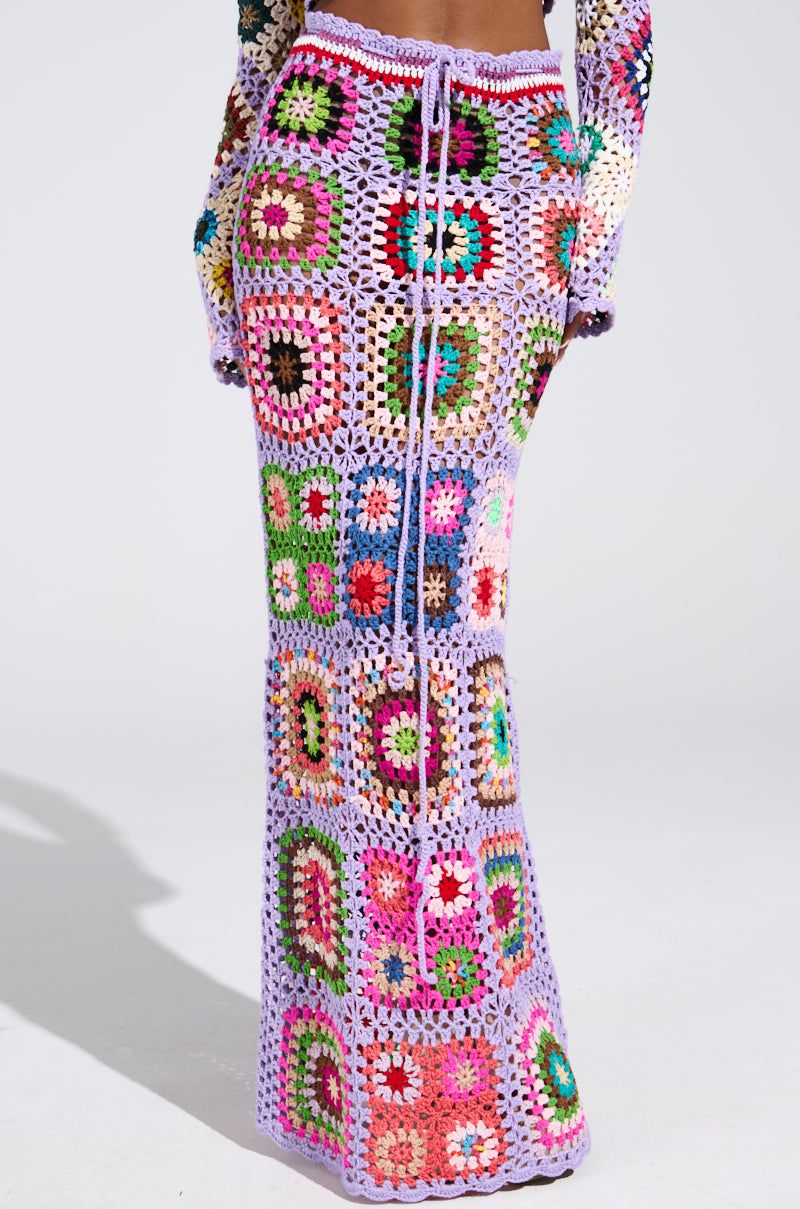 A person is showcasing the SHINE ON YOUR CROCHET MAXI SKIRT featuring a colorful granny square pattern and drawstring waist. The summer style includes vibrant hues like purple, green, red, and yellow. Paired perfectly with a crochet top, it offers an effortlessly chic high-rise fit.