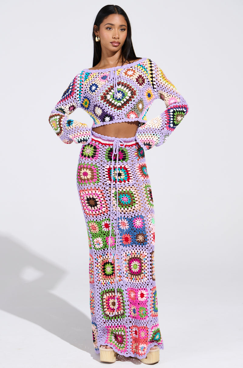 A woman poses confidently against a plain background in the SHINE ON YOUR CROCHET MAXI SKIRT, featuring a colorful patchwork of patterns. She pairs it with a vibrant crochet crop top, showcasing a perfect summer style outfit with her hands on her hips.