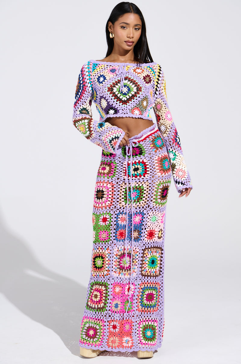 A woman confidently wears the "SHINE ON YOUR CROCHET MAXI SKIRT" set, featuring a vibrant patchwork design. The ensemble includes a cropped top and long skirt with a drawstring, epitomizing summer style as she poses against a plain background.