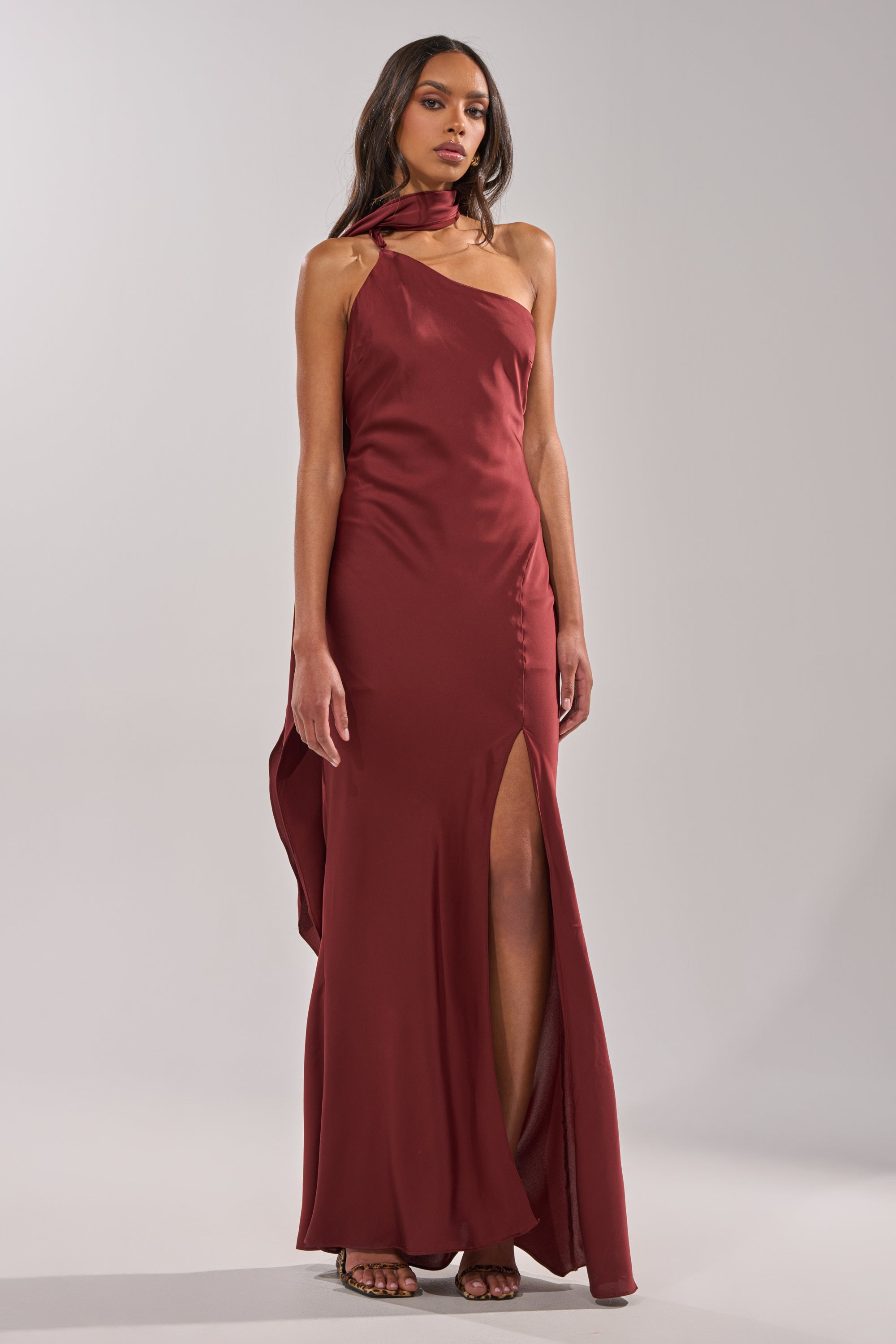 A woman in the RSVP READY SATIN MAXI DRESS, a wine-colored satin maxi with a side slit and matching scarf, stands against a plain light gray background. 0